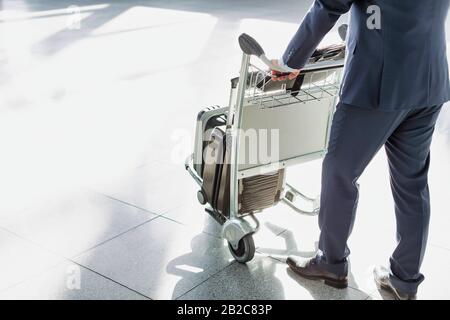 Mature businessman pushing luggage cart for check in at airport Stock Photo