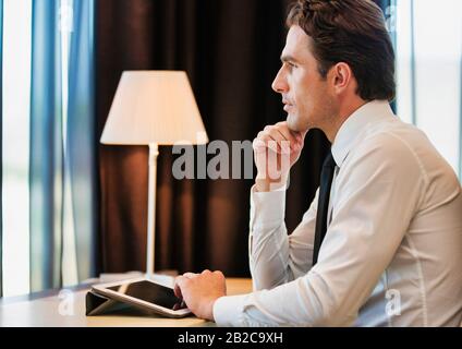 Thoughtful businessman using digital tablet while sitting with lens flare Stock Photo