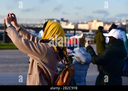 Chinese tourists in gauze masks take photographs with smartphones on excursions. Stock Photo