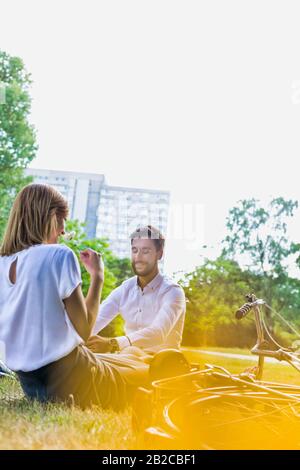 Young attractive business couple talking while sitting on the grass in park Stock Photo