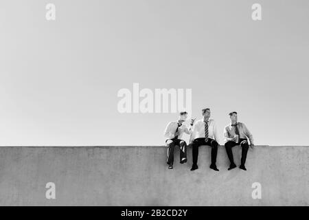 Black and white photo of thoughtful businessmen sitting and relaxing on rooftop Stock Photo