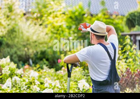 Rear view of tired male gardener leaning on shovel Stock Photo - Alamy