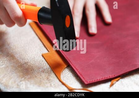 A leather craftsman produces leather goods. He taps the hammer. Handmade work. Stock Photo