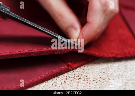 A leather craftsman works with leather. Sews leather goods. Making things handmade. Women's hands with a needle, thread, scissors and a blowtorch. Clo Stock Photo