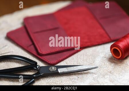 A leather craftsman works with leather. Sews leather goods. Making things handmade. Women's hands with a needle, thread, scissors and a blowtorch. Clo Stock Photo
