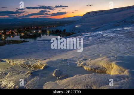 Illuminated white Pamukkale travertines in foreground (Turkey). Sunset over mountains in background. Stock Photo