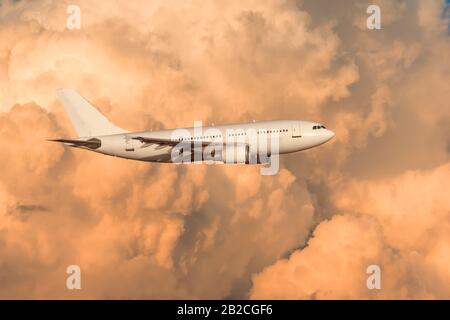 The plane flies on powerful cumulus clouds lit by the setting sun Stock Photo
