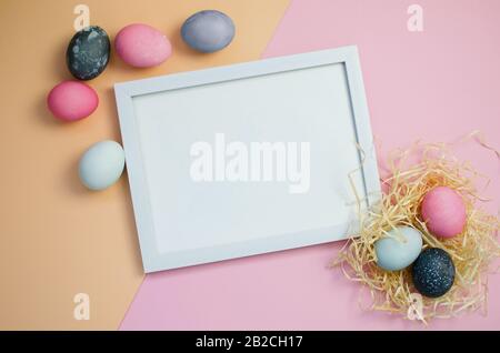 Painted colorful Easter eggs and gift on pink and yellow background and frame for text Stock Photo