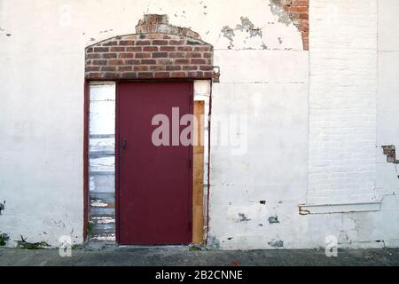 a white stucco wall at an alley building with a red door with exposed brick Stock Photo