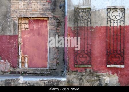 a red fadeing painted dirty warehouse in an alley with red door rusted and concrete steps Stock Photo