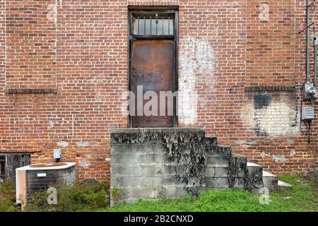 a beautiful old rusted warehouse door on a vintage red brick building with concrete steps and grass Stock Photo