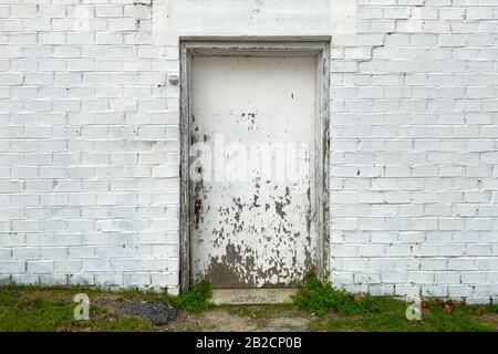 a back alley boarded up doorway with whitewashed brick building in an alley with grass path Stock Photo