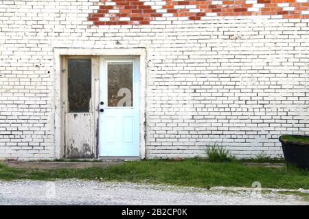 an abandoned painted white brick store doorway with exposed red brick Stock Photo