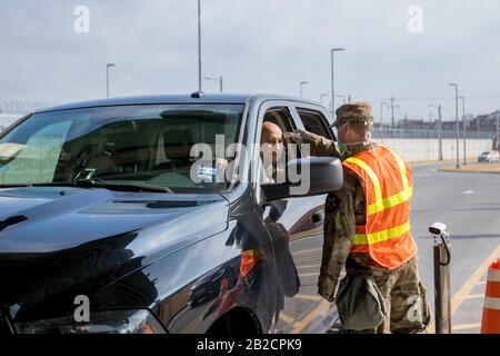 A U.S. soldier screens passengers for COVID-19, using a thermometer at an entry gate for Army Garrison Humphreys, February 27, 2020 in Pyeongtaek, South Korea. The outbreak of novel coronavirus in South Korea is second only to China. Stock Photo