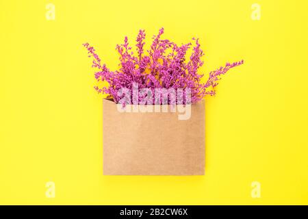Bright purple or violet lavender flowers in craft brown envelope with copy space isolated on yellow background. Trendy banner for Valentines Day or In Stock Photo