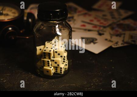 Bottle with dice on table in an underground casino on background of card and an abandoned alarm clock Stock Photo