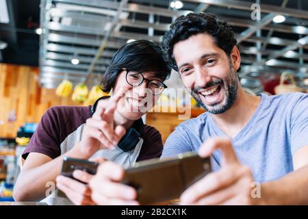 an Asian guy takes a cell phone selfie with his Caucasian friend Stock Photo