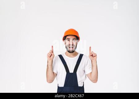 Photo of positive young man builder in helmet posing isolated over white wall background pointing aside. Stock Photo