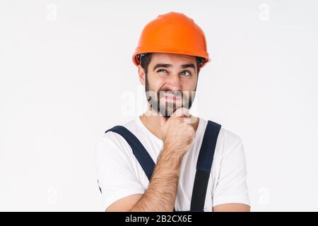 Photo of thinking thoughtful young man builder in helmet posing isolated over white wall background. Stock Photo