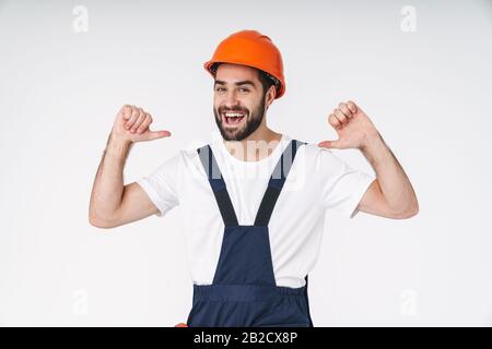 Photo of a cheery optimistic young man builder in helmet posing isolated over white wall background pointing to himself. Stock Photo