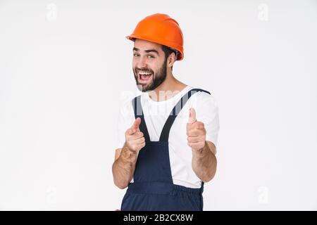 Photo of a cheery optimistic young man builder in helmet posing isolated over white wall background pointing to you. Stock Photo