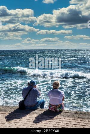 Elderly couple sitting and watching the waves Stock Photo