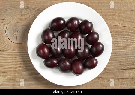 Plums in plate on wooden background, top view Stock Photo
