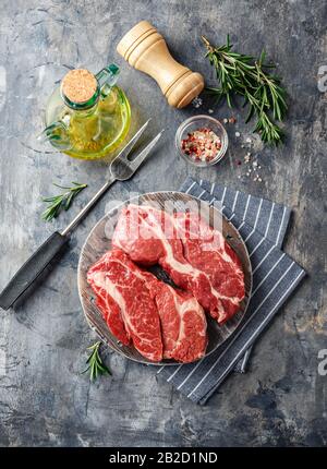 Two Fresh Raw meat Prime Black Angus Chuck roll steak on a wooden cutting board on a gray background. View from above. Stock Photo