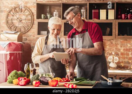 Elderly couple using digital tablet in kitchen, looking for new recipes Stock Photo