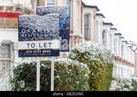 London, UK - December 10, 2019 - To Let sign covered by winter snow around West Hampstead area with terrace houses in the background Stock Photo