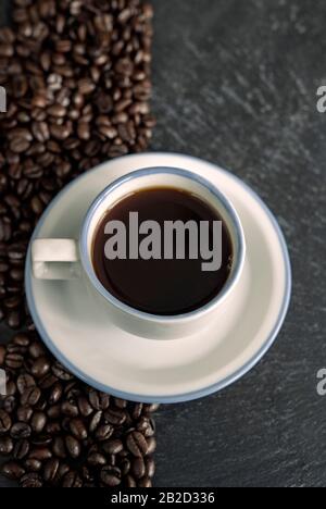 Cup of black coffee on a table, surrounded by coffee beans on one side Stock Photo