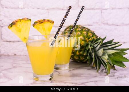 Two glasses of fresh pineapple juice and pineapple on a table on a white background. Stock Photo