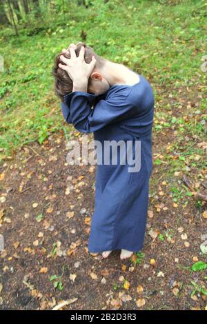 Syktyvkar, Russia - september, 2019: a woman of european appearance with short dark hair, dressed in a blue robe, performs a pagan witchcraft ritual. Dark forest on background. Stock photography. Stock Photo