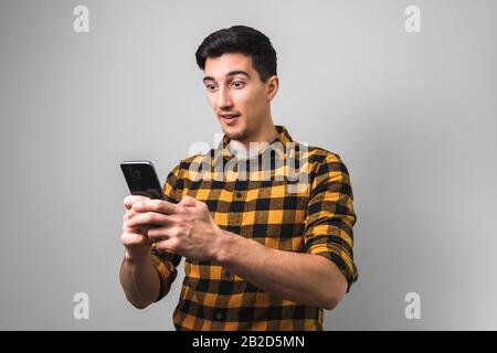 young man in yellow shirt looking in phone surprised by a post or news Stock Photo