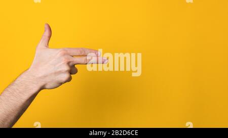 man hand imitating gun over a wide yellow background with copyspace Stock Photo