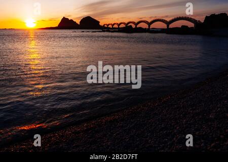 A small island off the coast and the iconic eight-arch footbridge silhouetted during sunrise, at Sanxiantai in Taitung, Taiwan Stock Photo