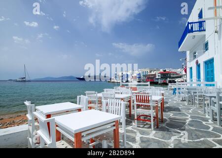 Outdoor restaurant with sea view near romantic colorful Little Venice at sunny day. Yachts on Aegean sea. Amazing touristic place, People walking alon Stock Photo