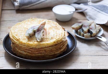 Pancakes with glavraks from mackerel and sour cream on a wooden background. Stock Photo
