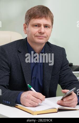 Mature man sitting in his office writing in notepad Stock Photo