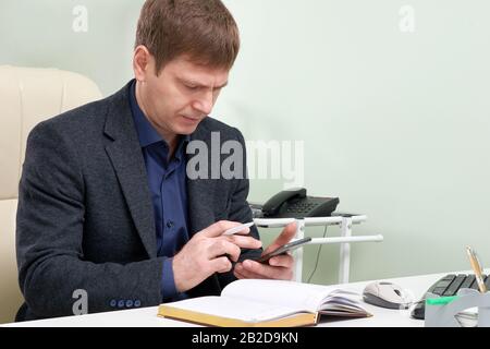 Mature man sitting in his office texting on smart phone Stock Photo