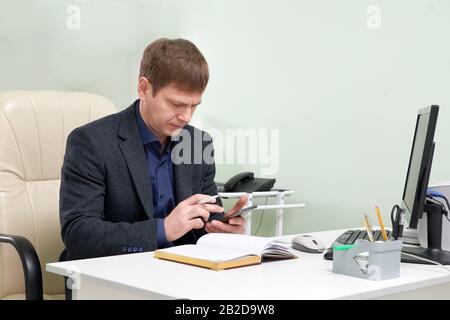 Mature man sitting in his office texting on smart phone Stock Photo