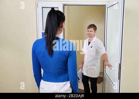 Doctor welcoming a woman patient to his office opening door in modern clinic Stock Photo