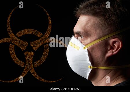 side view / profile of a young man wearing a protective mask in dark atmosphere - orange biohazard sign / emblem in the background Stock Photo