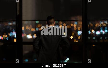 Businessman Standing Near Window Looking At City View In Office Stock Photo