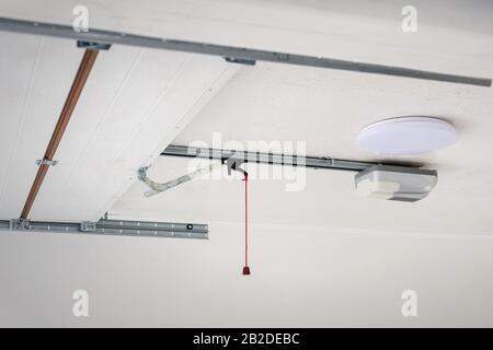 Opening door and automatic garage door opener electric engine gear mounted on ceiling with emergency cord. Double place empty garage interior with Stock Photo
