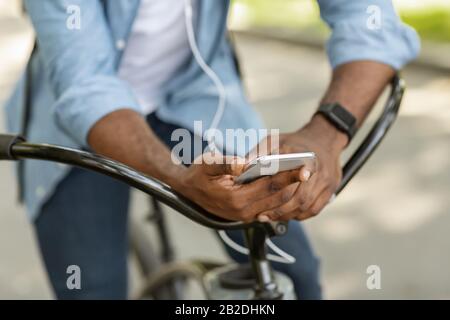 Unrecognizable man on bicycle holding smartphone and listening music in earphones Stock Photo