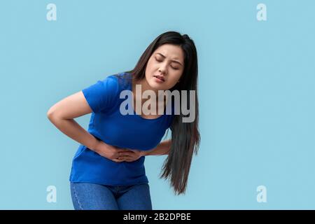 Coronavirus Concept. Chinese woman standing isolated on grey having stomachache wincing unhappy Stock Photo