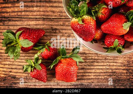 Overhead shot of Fresh Strawberries in a white china bowl on wooden surface with a few loose strawberries at the side Stock Photo