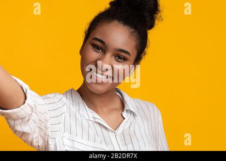 Pretty Afro Girl Taking Selfie, Making Self-Portrait, Posing Over Yellow Background Stock Photo