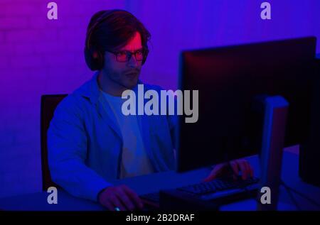 Gamer At Computer Playing Shooter Games Sitting In Dark Room Stock Photo